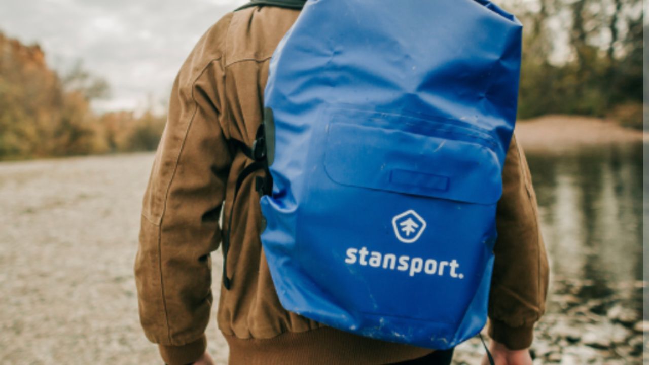 Person carrying blue Stansport waterproof dry bag backpack by river.